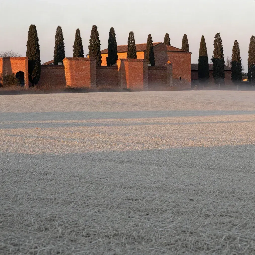 Paesaggio della pianura modenese con fabbrica in mattoni rossi e cipressi nella luce serale.